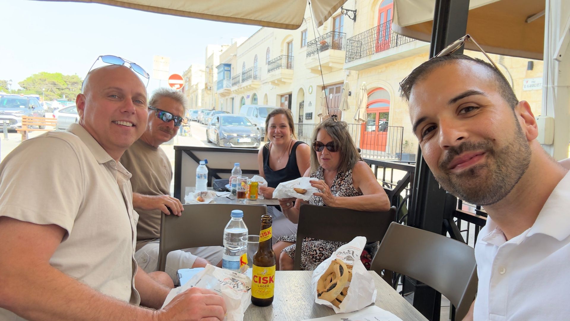Group of people enjoying a meal outside at a cafe with food and drinks on the table.